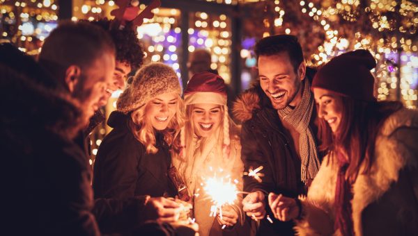 Three couple with sparklers enjoying Christmas outdoor party in the city street at night and with a lot of lights on background.