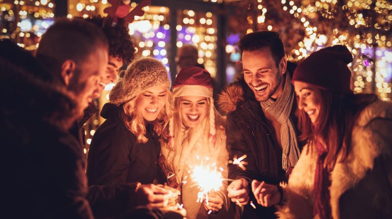 Three couple with sparklers enjoying Christmas outdoor party in the city street at night and with a lot of lights on background.